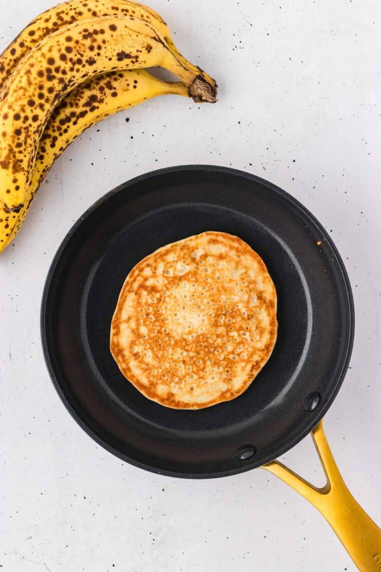 A banana pancake cooking in a skillet