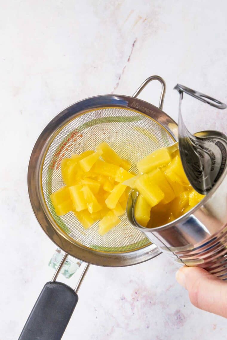 A can of pineapple being drained in a strainer.