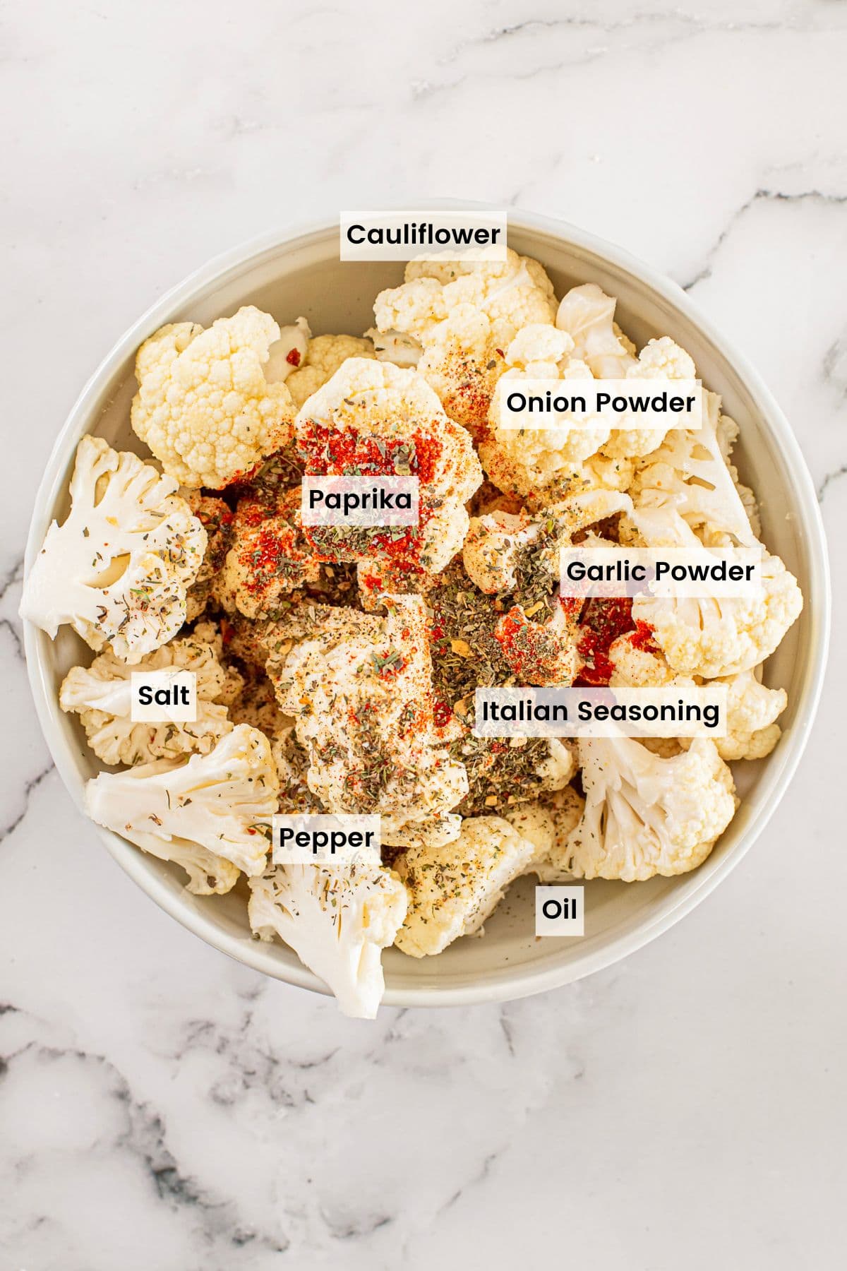 A bowl of cauliflower florets with seasonings sprinkled on top and text labels of the ingredients.