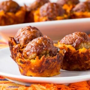 Sweet potato bites topped with barbecue sauce-coated meatballs on a plate.