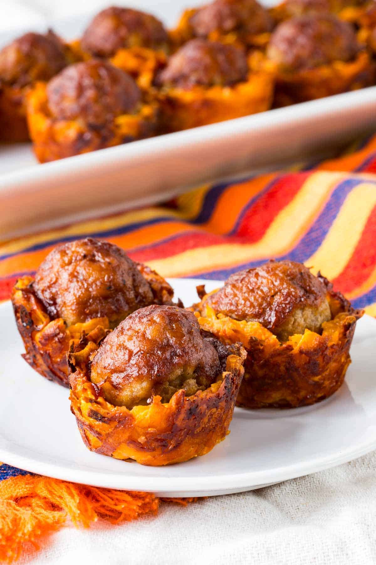 Three small sweet potato cups each topped with a meatball on a small white plate.
