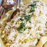 A spoon resting in a bowl of cauliflower colcannon with shredded brussels sprouts and parsley on top.