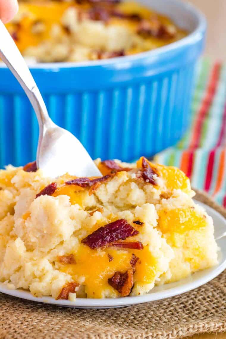 A fork in a scoop of mashed cauliflower on a plate.
