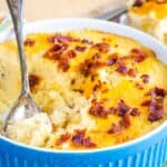 A serving spoon resting in a baking dish of cheesy mashed cauliflower bake with bacon.