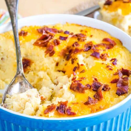 A serving spoon resting in a baking dish of cheesy mashed cauliflower bake with bacon.