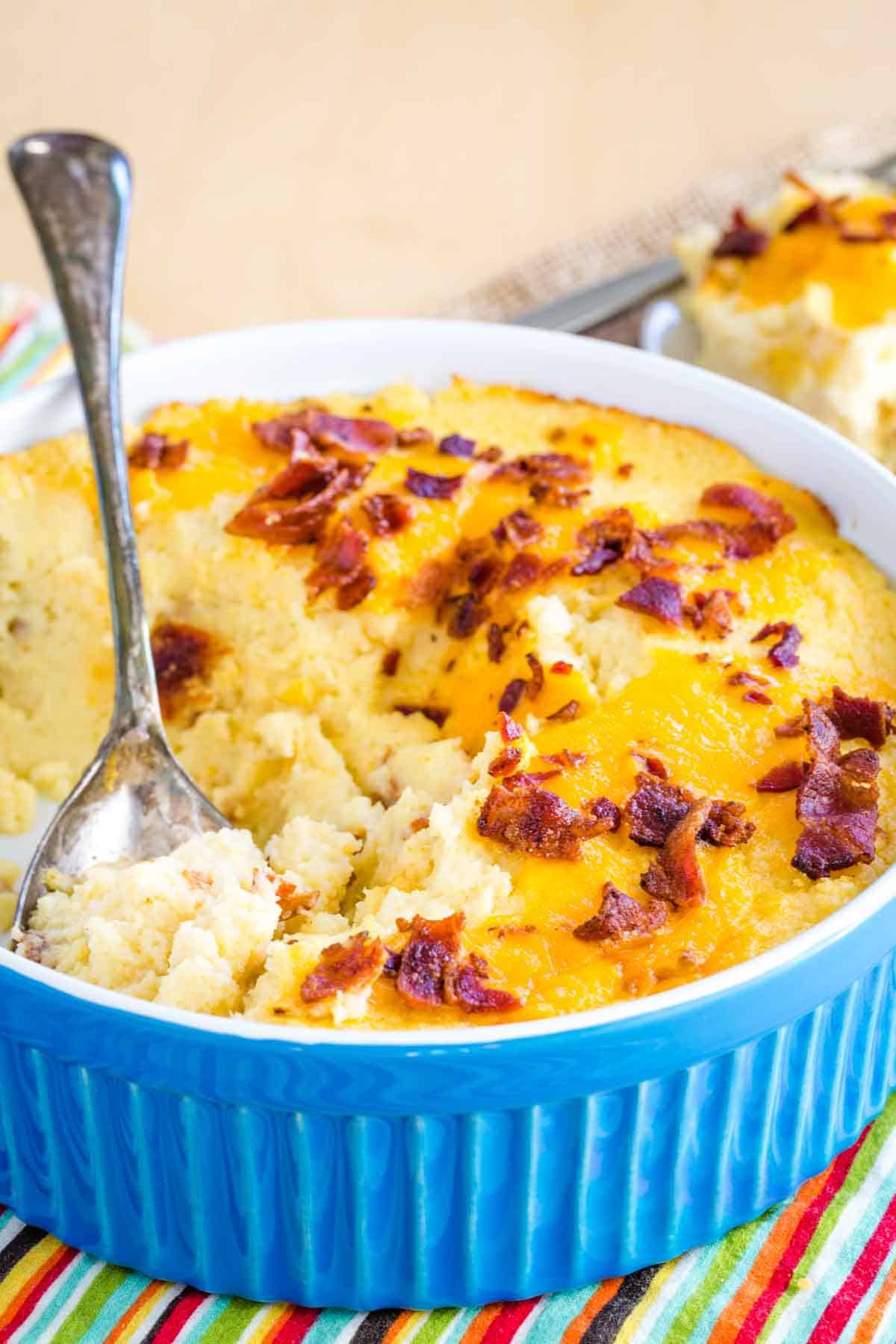 A serving spoon resting in a baking dish of cheesy mashed cauliflower bake with bacon.