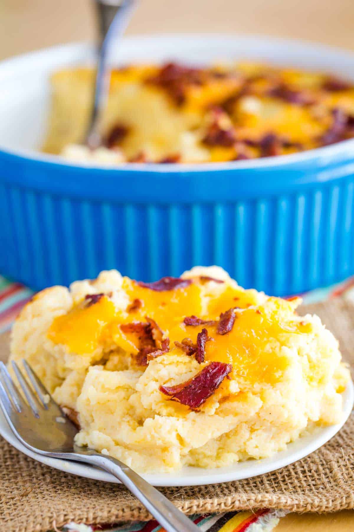 Mashed cauliflower topped with bacon and cheese on a plate with a fork resting on it.