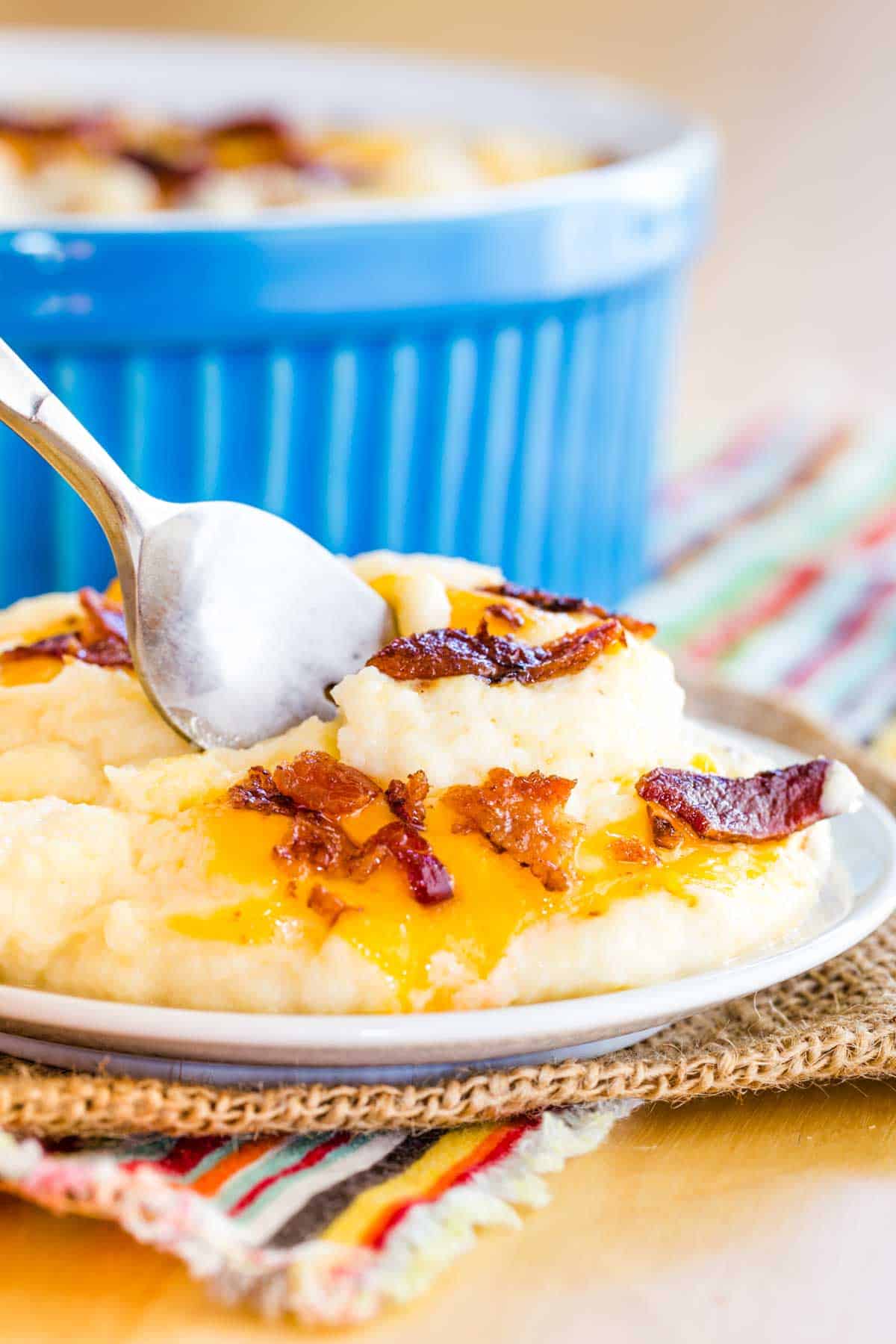A fork in a scoop of creamy cauliflower mash with bacon and cheese on a plate.