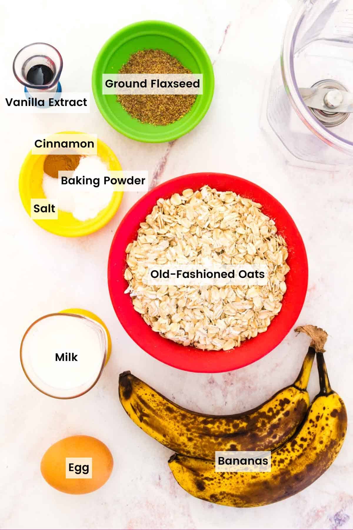 A couple of overripe bananas and the other waffle ingredients in bowls and measuring cups on a marble countertop with text labels.