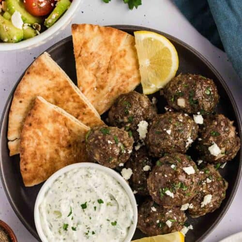 Overhead view of a black plate of Greek meatballs with pita and tzatziki