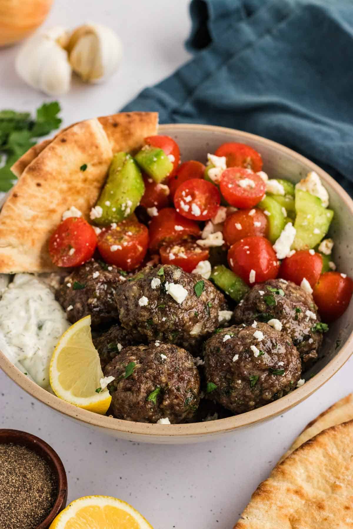 A bowl of Greek meatballs with salad, pita, and tzatziki