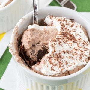 A spoon in a ramekin of Bailey's mousse pie topped with whipped cream.