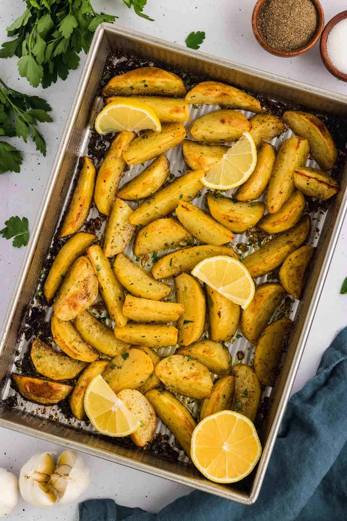 Potatoes are baked in a lemony, garlicky broth until golden on the outside and soft on the inside in this Greek Potatoes recipe. Overhead view of a sheet pan of Greek potatoes with lemon slices