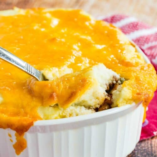 A spoon digging into a cheese topped casserole.