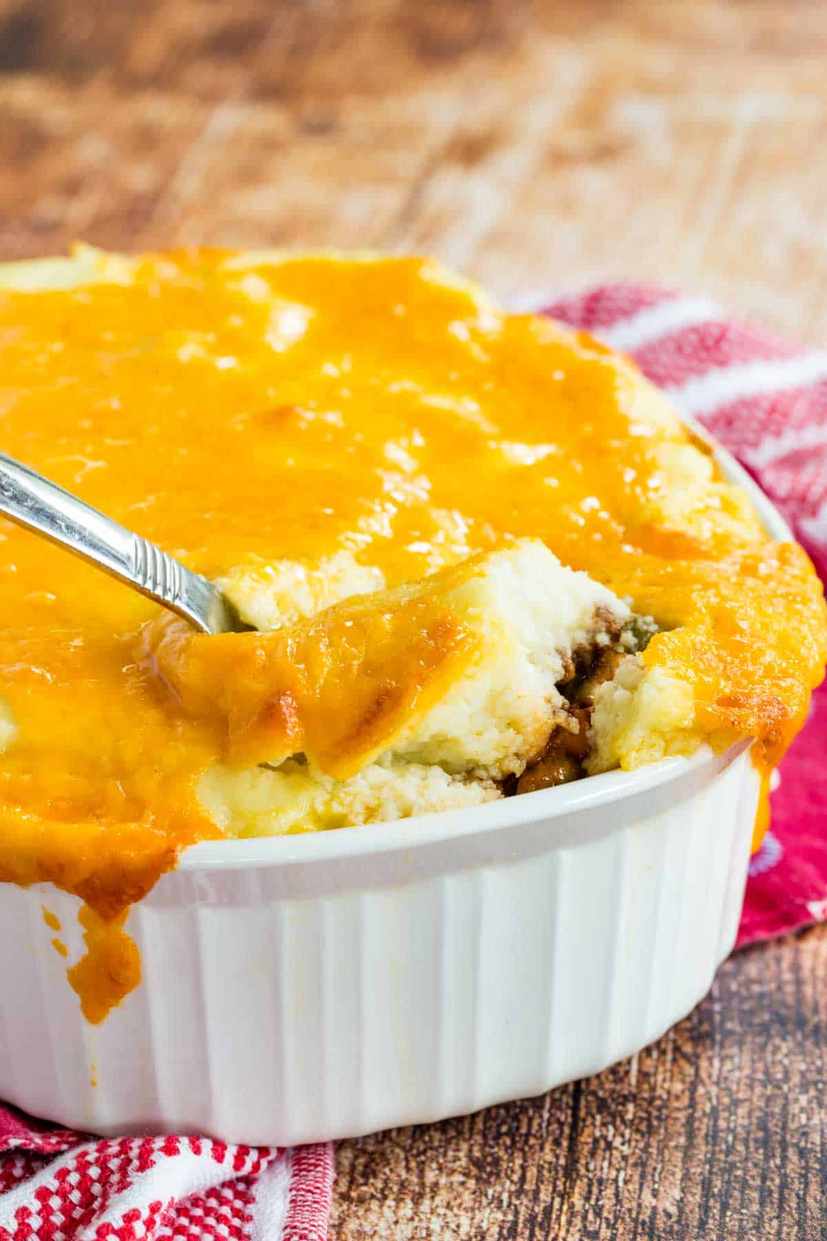 A spoon digging into a cheese topped casserole.