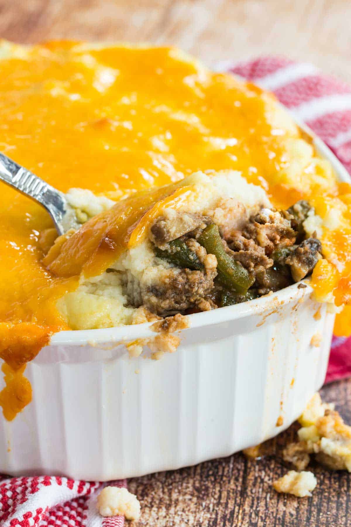 Shepherds pie topped with cauliflower mash and melted cheese being scooped out of a casserole dish.