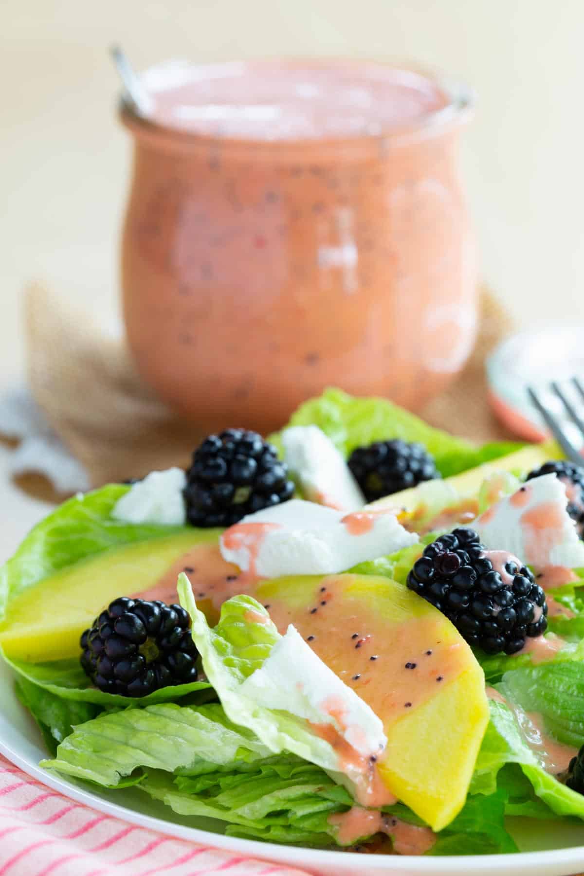 A blackberry mango goat cheese salad with strawberry poppyseed dressing on a plate.