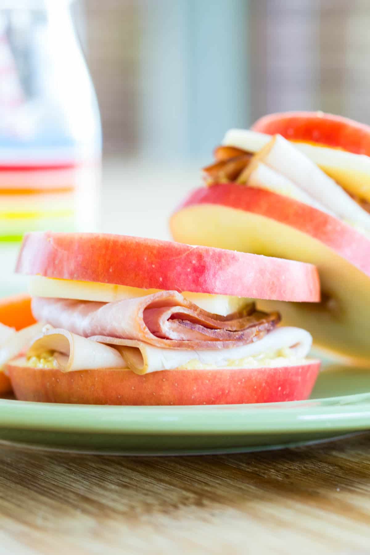 Apple slices stacked with deli meat and cheese to make a sandwich.