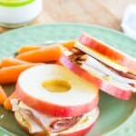Two small apple slice sandwiches on a plate with baby carrots.