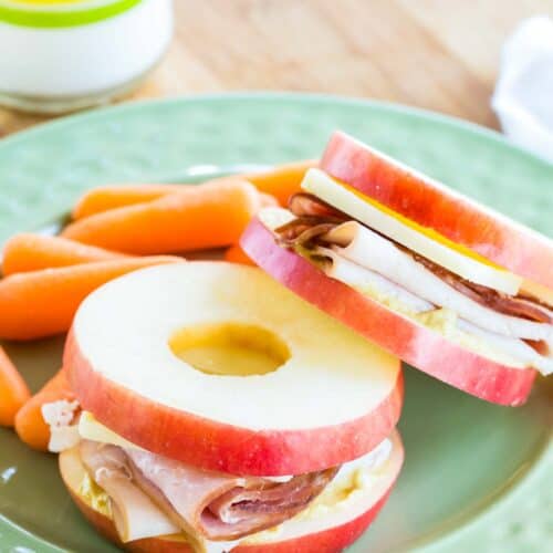 Two small apple slice sandwiches on a plate with baby carrots.