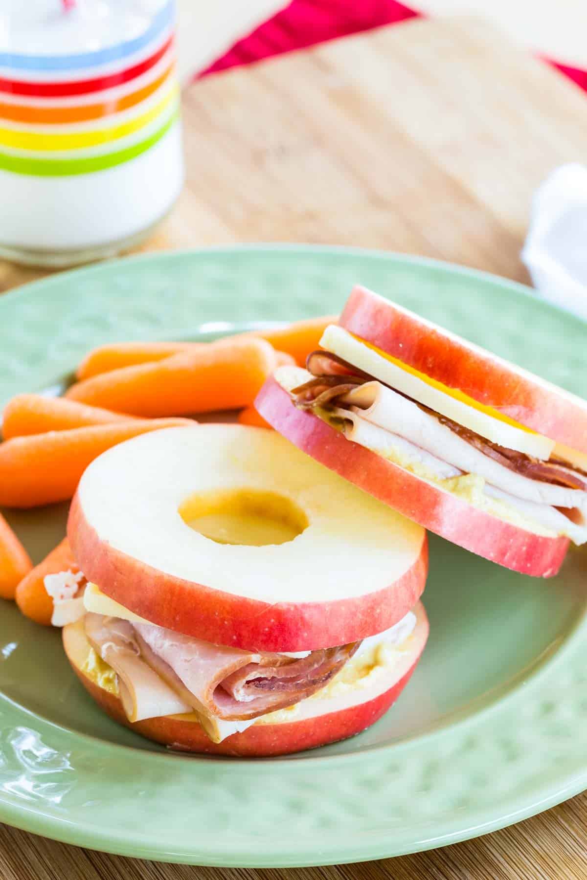 Two small apple slice sandwiches on a plate with baby carrots.