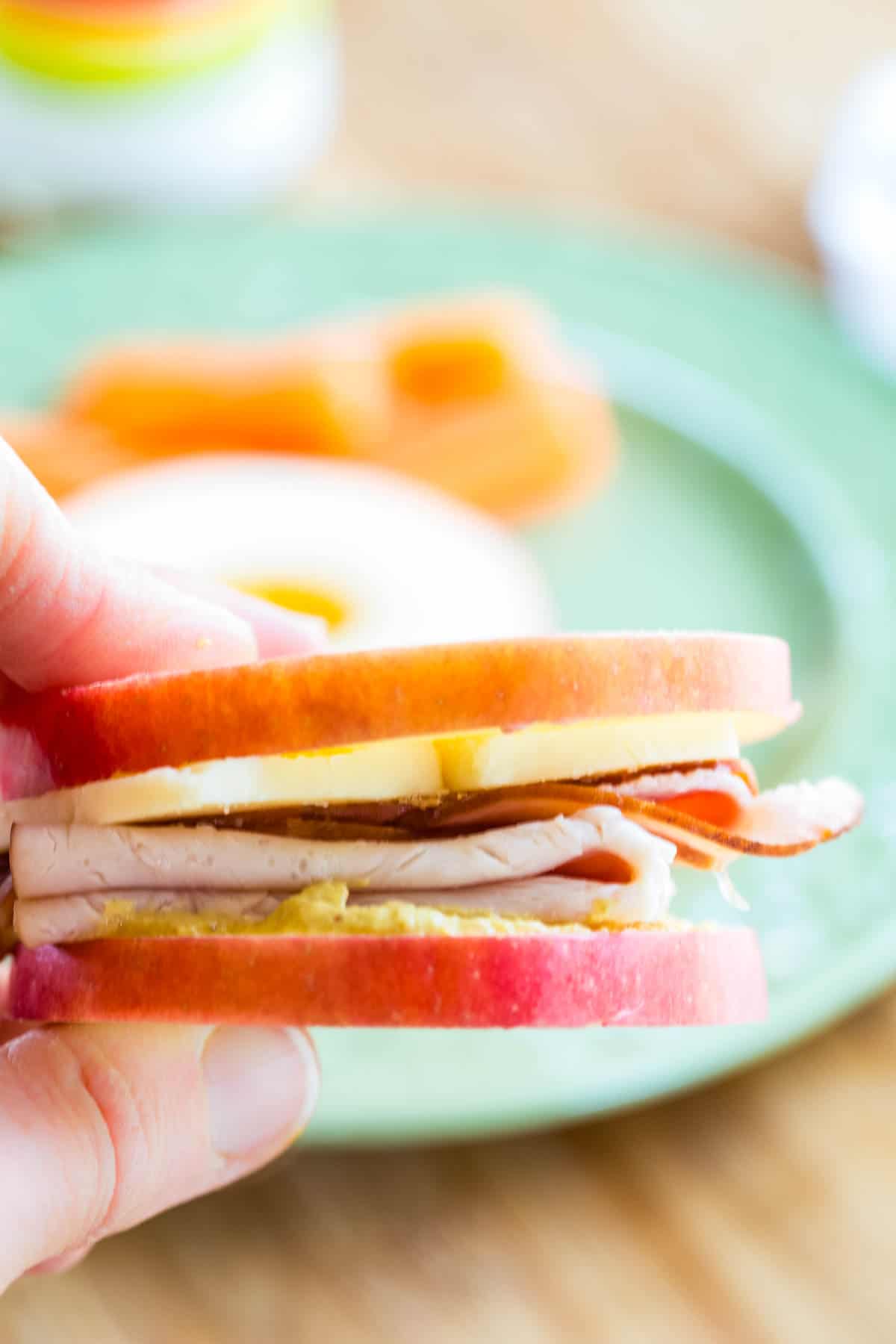 A hand holding an apple slice sandwich with deli meat.
