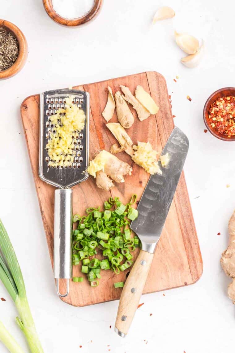 This easy sweet and spicy chicken is full of flavor, with honey, brown sugar, and sriracha. Ready in just 20 minutes! Grated garlic, ginger, and sliced green onion on a cutting board