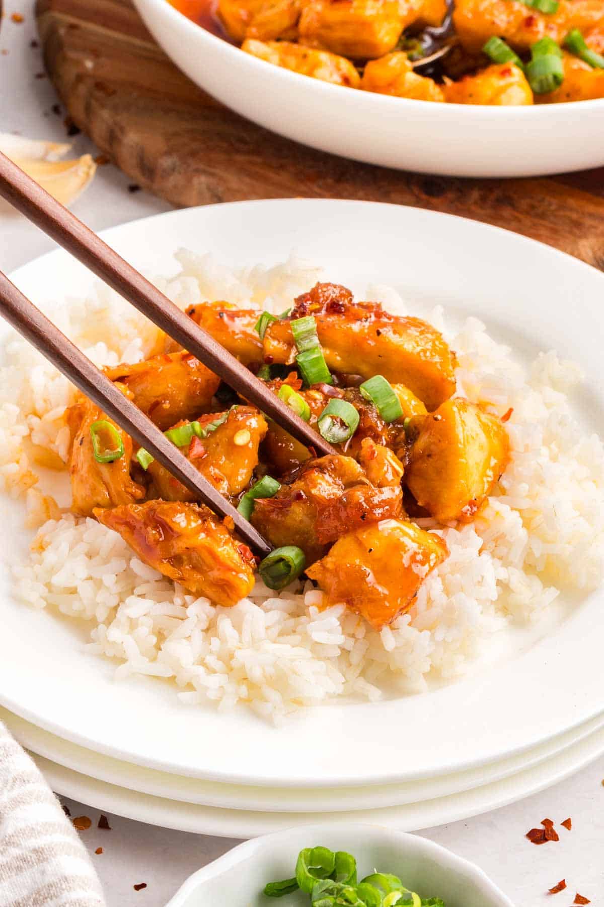 This easy sweet and spicy chicken is full of flavor, with honey, brown sugar, and sriracha. Ready in just 20 minutes! Chopsticks picking up a piece of sweet and spicy chicken from a bed of rice