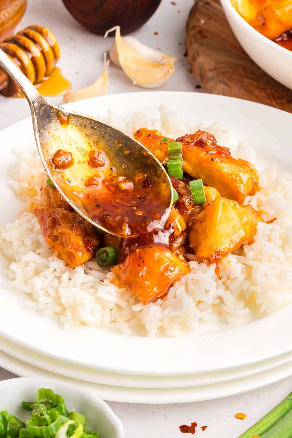This easy sweet and spicy chicken is full of flavor, with honey, brown sugar, and sriracha. Ready in just 20 minutes! Spooning sauce over sweet and spicy chicken on a bed of rice