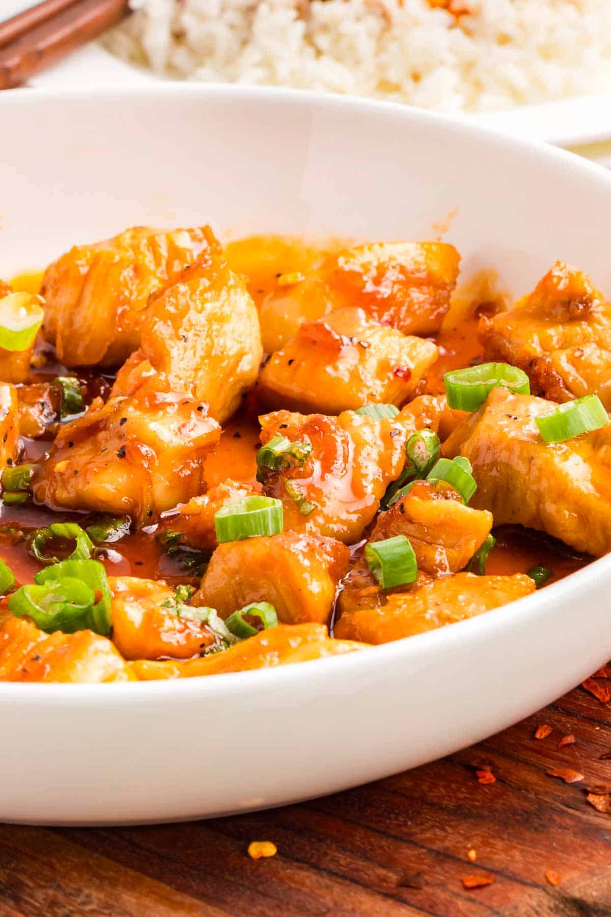 This easy sweet and spicy chicken is full of flavor, with honey, brown sugar, and sriracha. Ready in just 20 minutes! A white bowl of sweet and spicy chicken