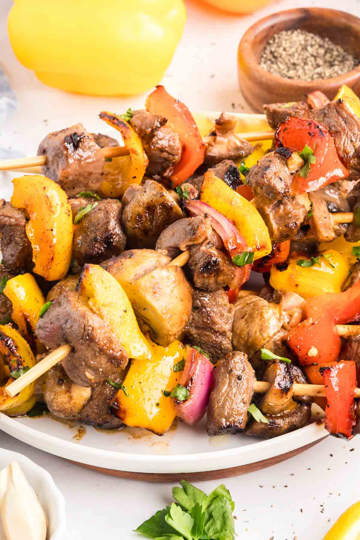 Chunks of sirloin are marinated then threaded onto skewers with onions, bell peppers, and mushrooms to make these beef kebabs. A pile of beef kebabs on a white plate