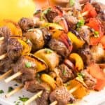 Angled side view of beef kebabs stacked on a white plate