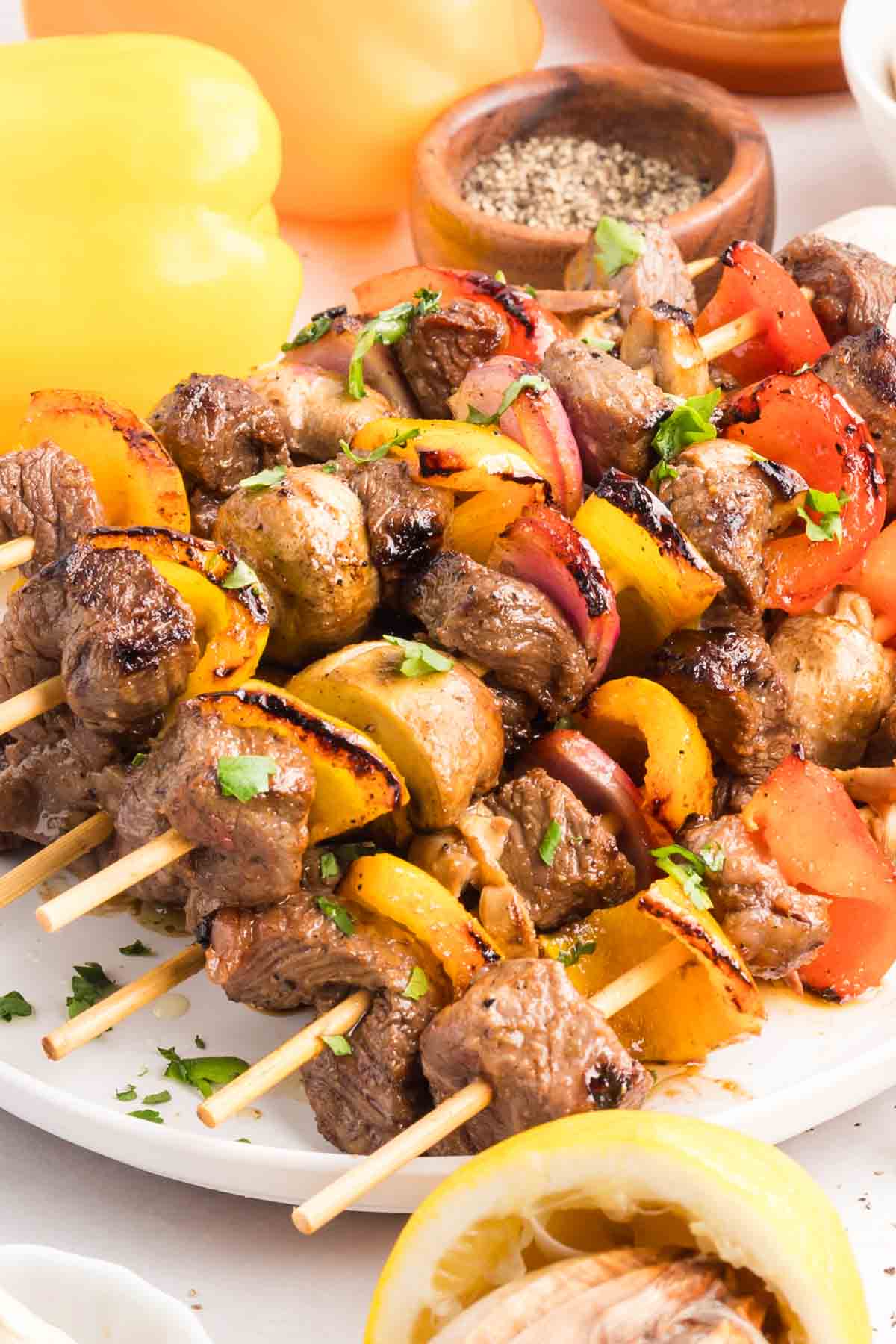 Chunks of sirloin are marinated then threaded onto skewers with onions, bell peppers, and mushrooms to make these beef kebabs. Angled side view of beef kebabs stacked on a white plate