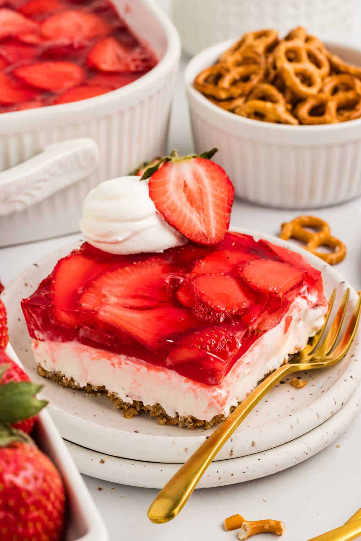 A slice of strawberry pretzel salad on a white plate with a gold fork