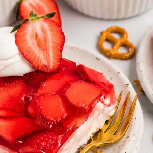 A slice of strawberry pretzel salad on a white plate with a gold fork
