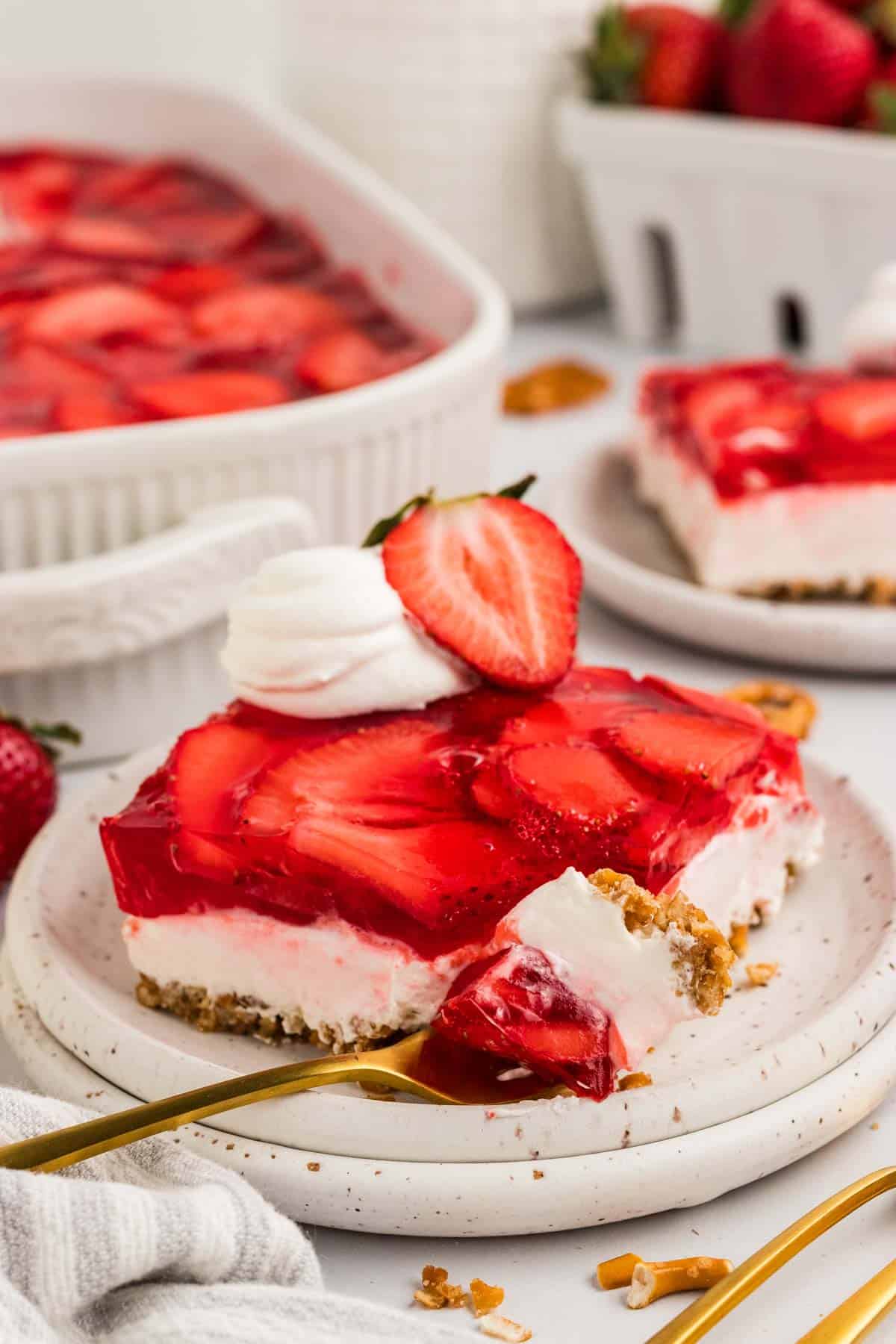 A slice of strawberry pretzel salad on a white plate with a bite on a fork next to it