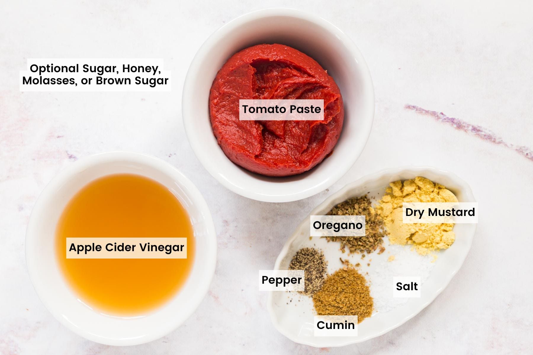 The ingredients to make homemade ketchup in bowls with text labels, including Apple Cider Vinegar, Tomato Paste, Black Pepper, Cumin, Salt, Dried Oregano, and Dry Mustard.