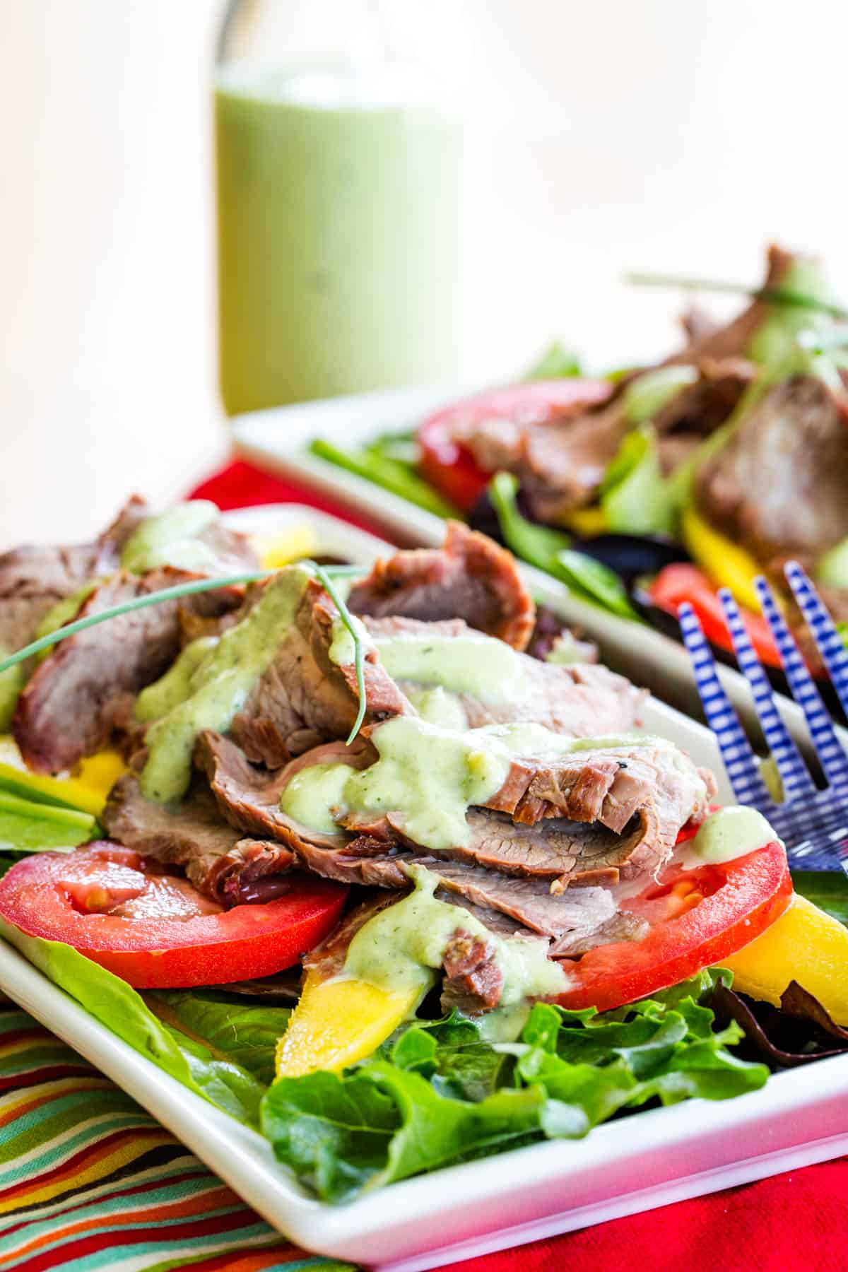 A mango steak salad with tomatoes and avocado ranch on a plate.