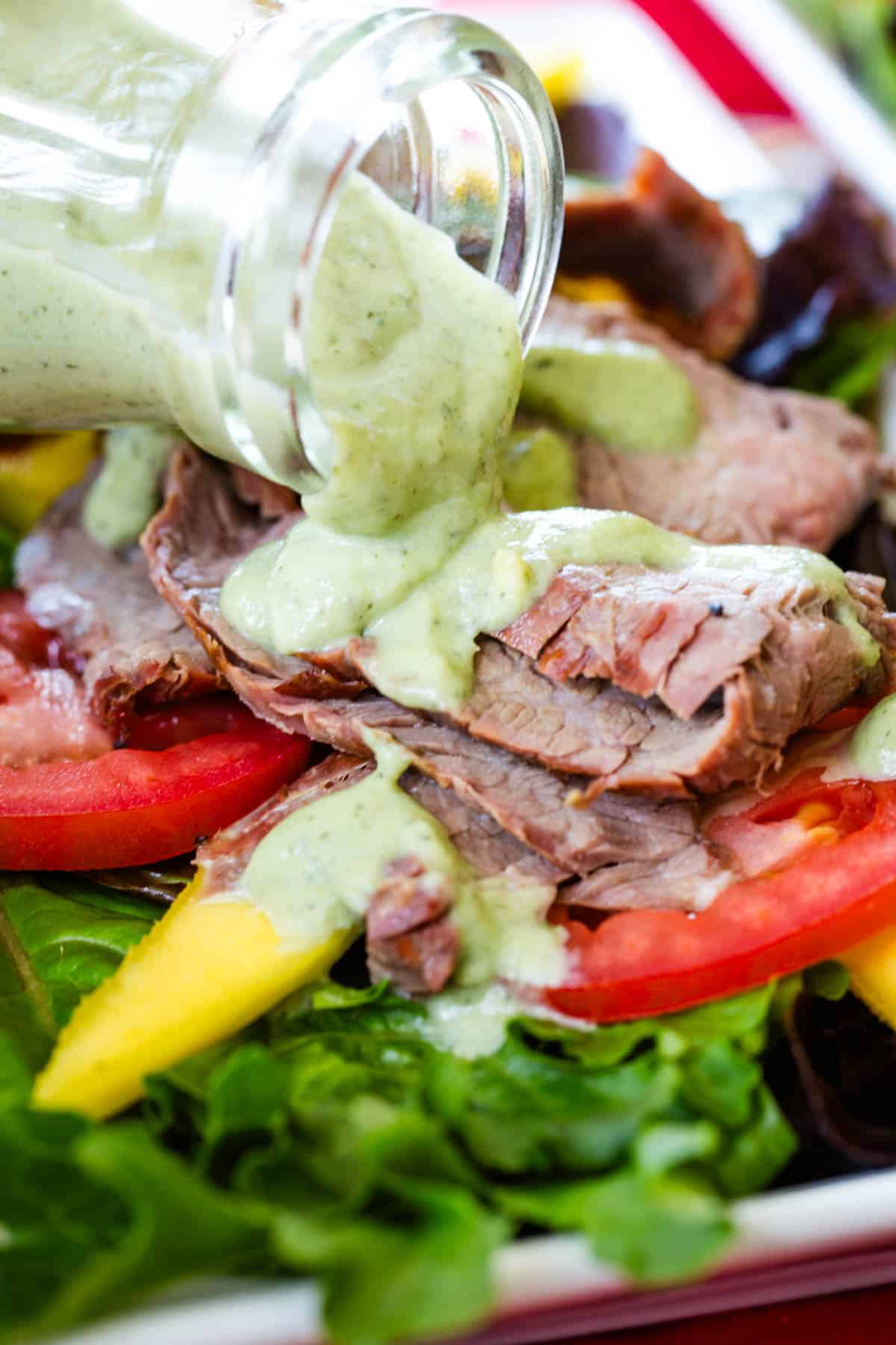 Avocado ranch being poured over steak on top of a salad.