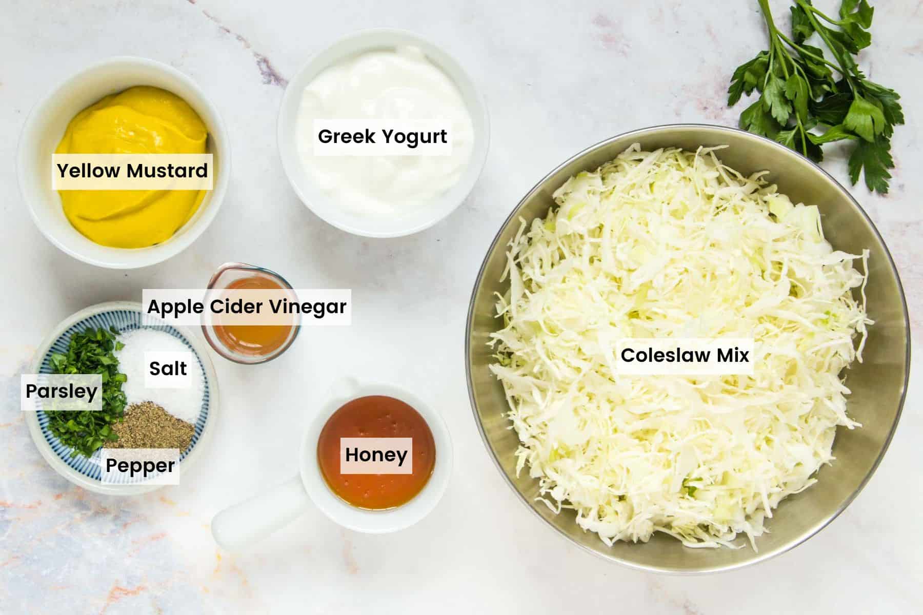 The ingredients for homemade mustard coleslaw in bowls on a countertop with text labels.