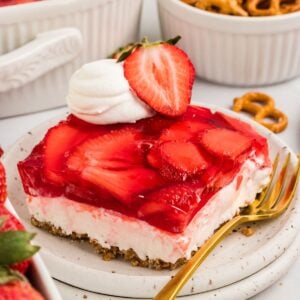 A slice of gluten free strawberry pretzel salad next to a gold fork on a white plate