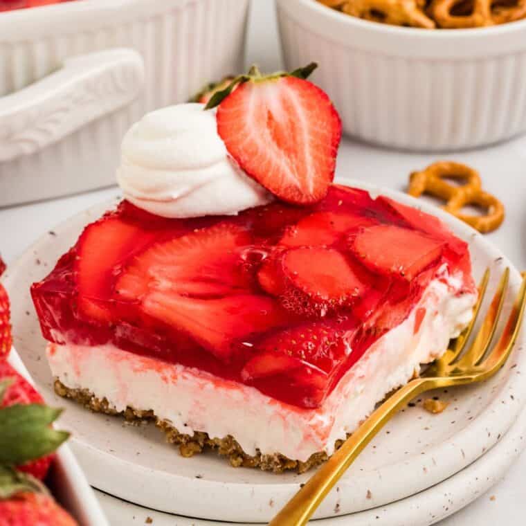 A slice of gluten free strawberry pretzel salad next to a gold fork on a white plate