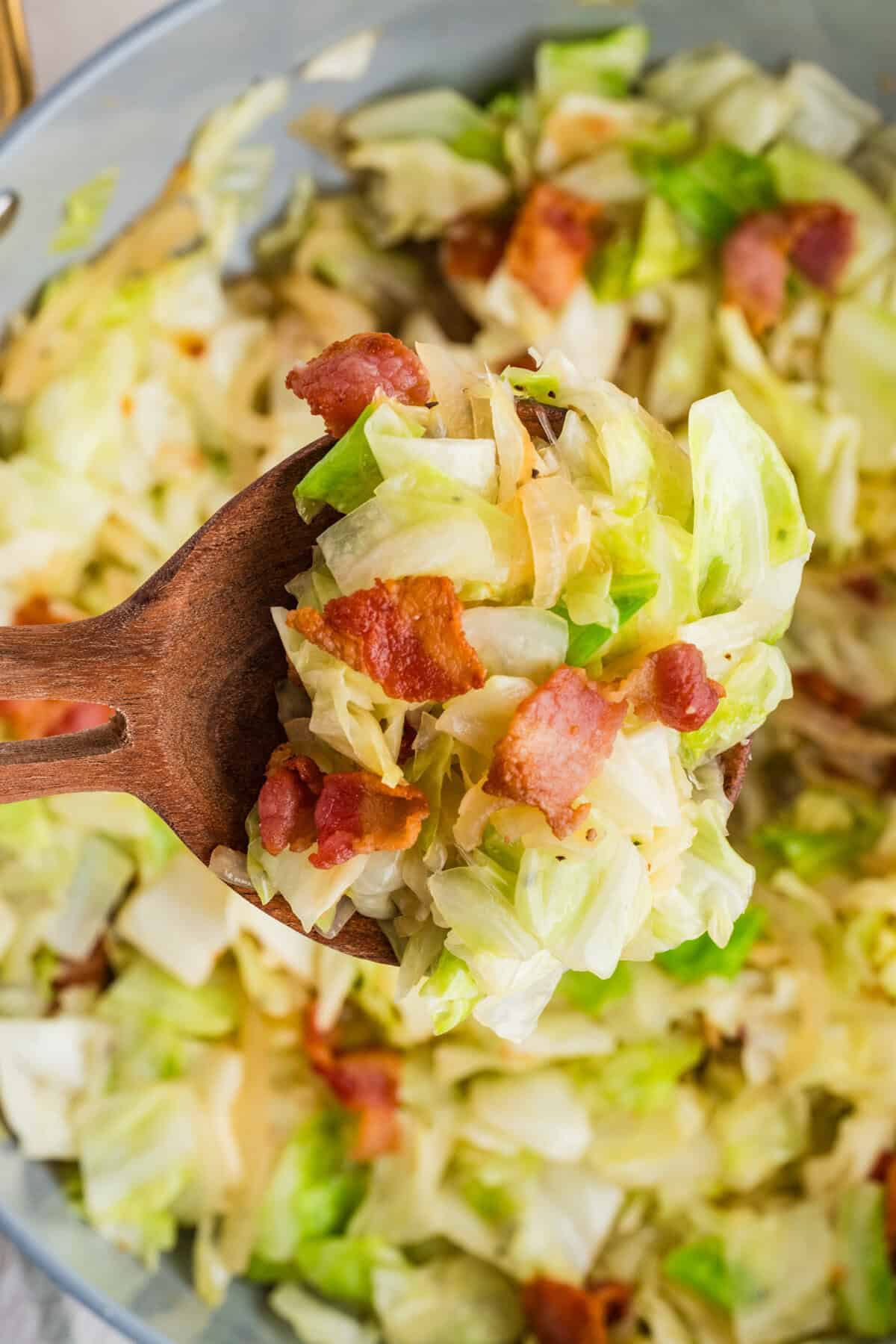 This easy Fried Cabbage recipe turns a handful of ingredients into a savory side dish perfect for busy weeknights & potlucks. Fried cabbage on a wooden spoon above a bowl