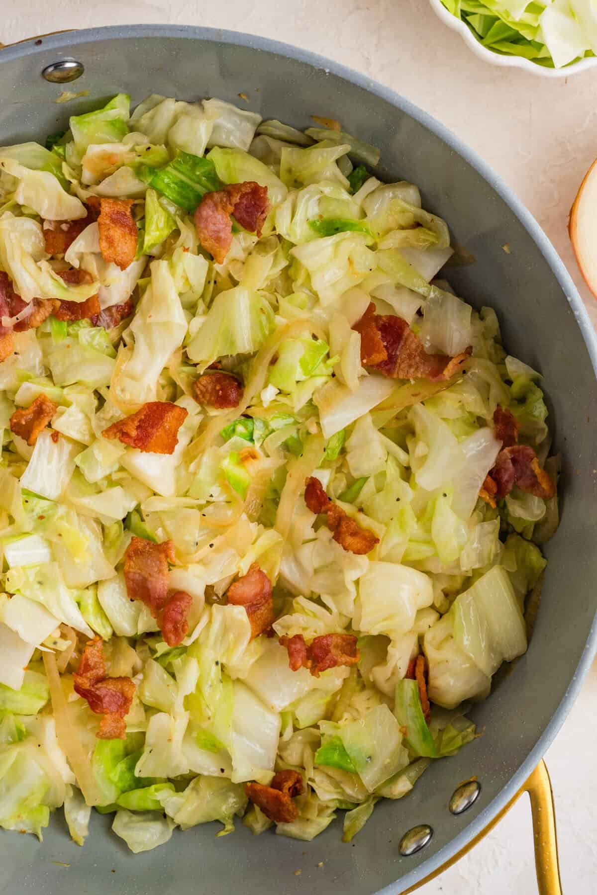 This easy Fried Cabbage recipe turns a handful of ingredients into a savory side dish perfect for busy weeknights & potlucks. Overhead view of fried cabbage and bacon in a skillet