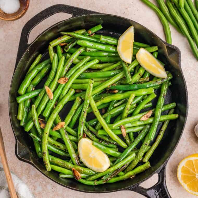 Overhead view of a skillet of garlic green beans with lemon wedges