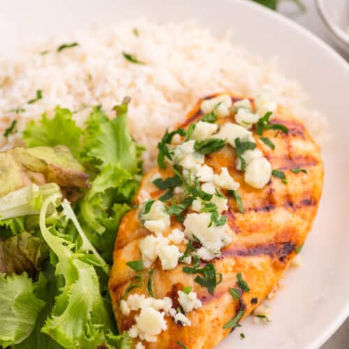 A grilled buffalo chicken breast on a plate with rice and salad