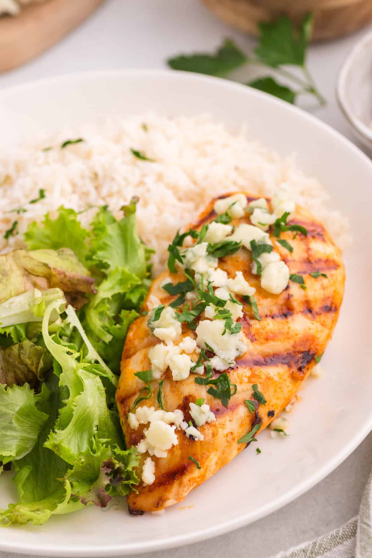 A grilled buffalo chicken breast on a plate with rice and salad