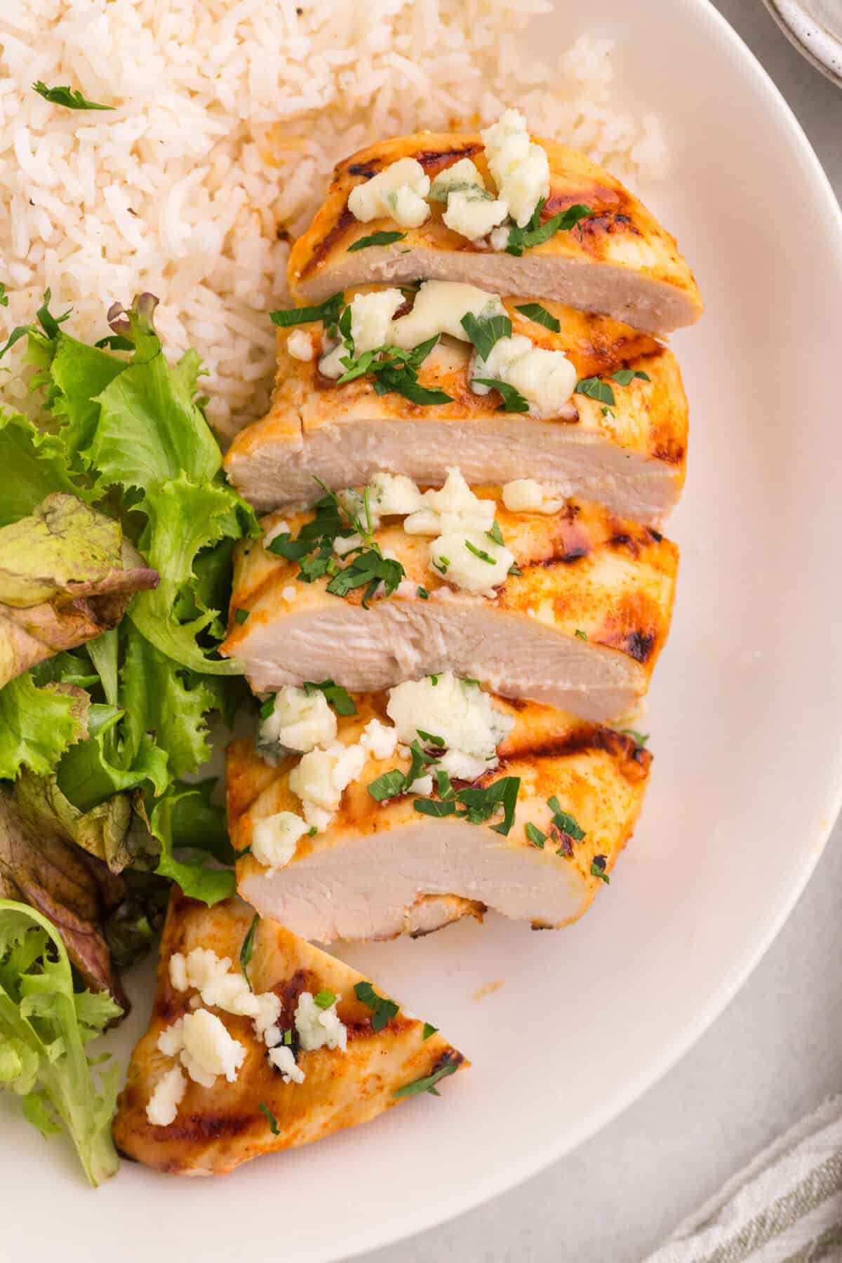 A grilled buffalo chicken breast sliced on a plate and topped with blue cheese crumbles