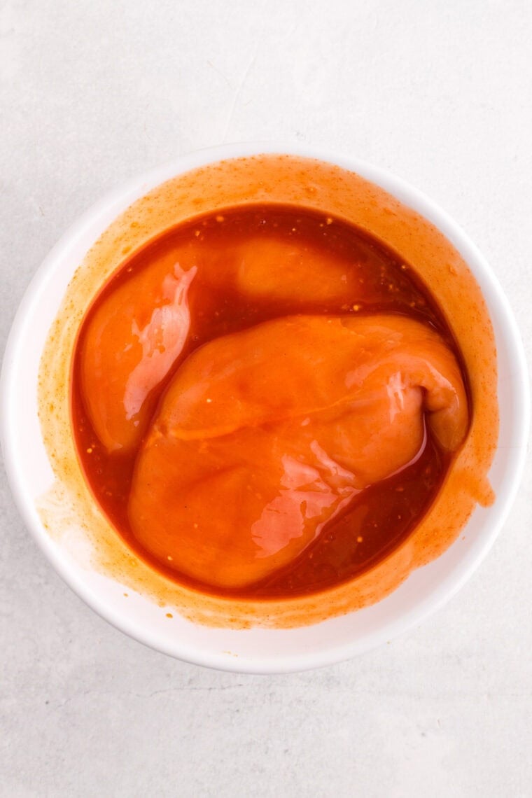 Chicken breasts marinating in a bowl of buffalo sauce
