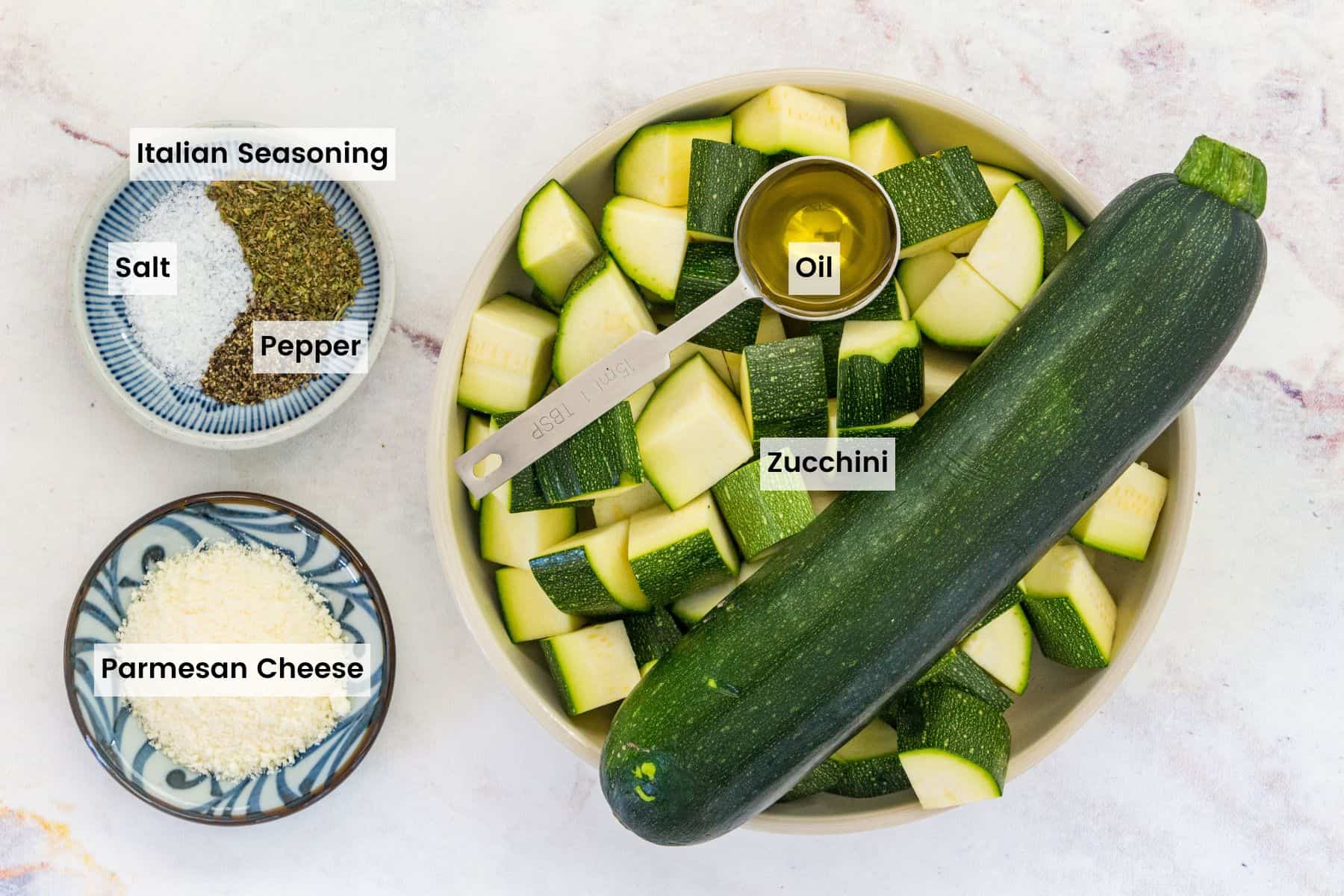 The ingredients for air fryer zucchini with text labels including: zucchini, oil, salt, pepper, Italian seasoning, and parmesan cheese.